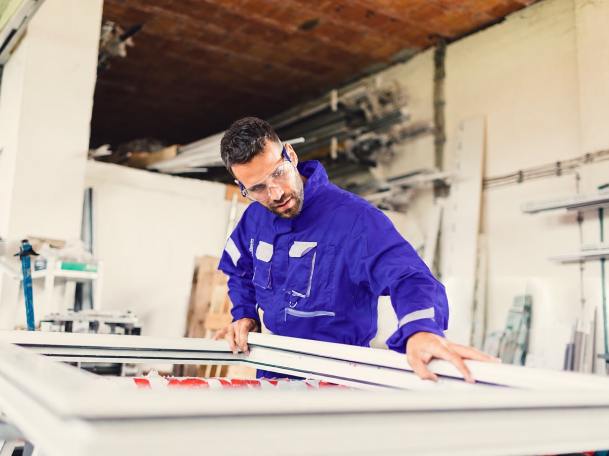 Worker in safety glasses inspecting a window frame on the shop floor