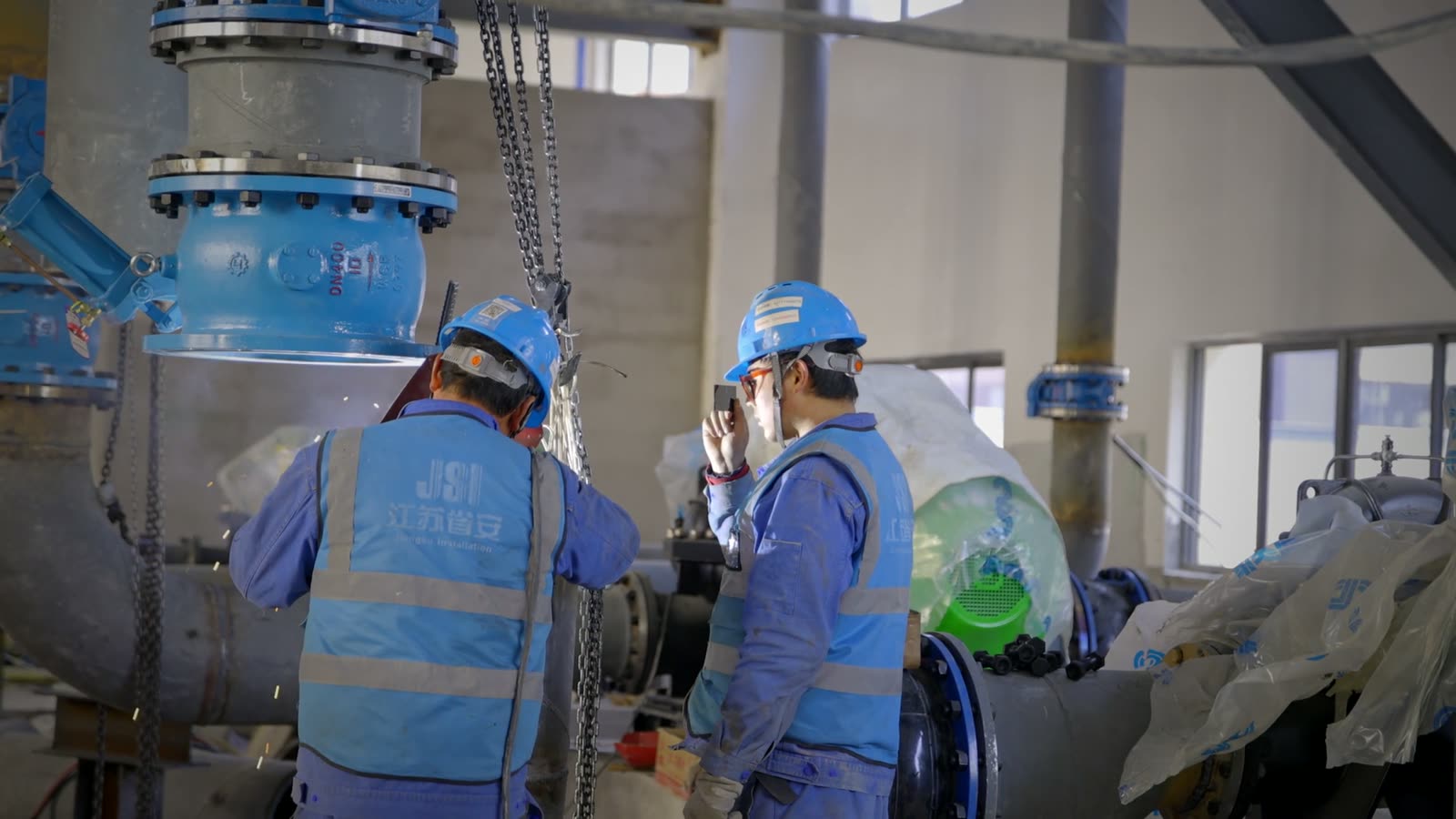 Two engineers in hard hats working on a pump together