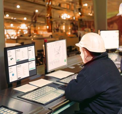 Image depicting a plant worker looking at a dashboard from a control room.